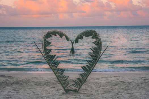 Palm tree branches are tied into the shape of a heart, on a quiet beach on the island of Koh Pha Ngan, Thailand .