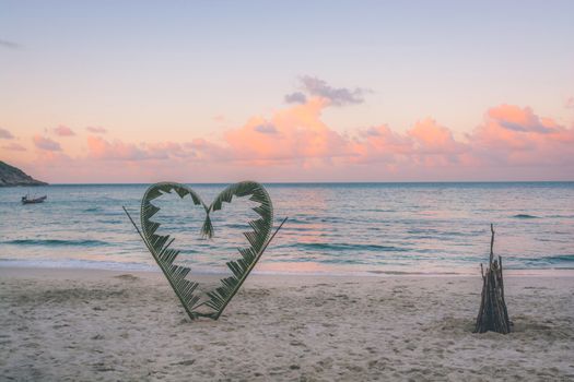 Palm tree branches are tied into the shape of a heart, on a quiet beach on the island of Koh Pha Ngan, Thailand .