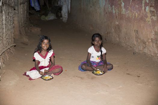 Documentary editorial image. Pondicherry, Tamil Nadu, India - April 24 2014. Very poor young girl sitting in the street, eating on the floor during the night. Poverty