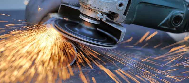 Worker cutting metal with grinder. Sparks while grinding iron