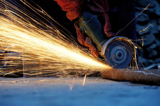 Worker cutting metal with grinder. Sparks while grinding iron