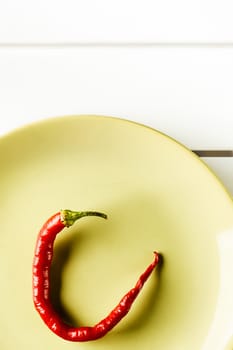 Top view red hot pepper on green dish over white wood. Vertical image.