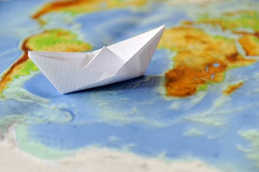 Paper boat on a background map of the world. Traveling concept