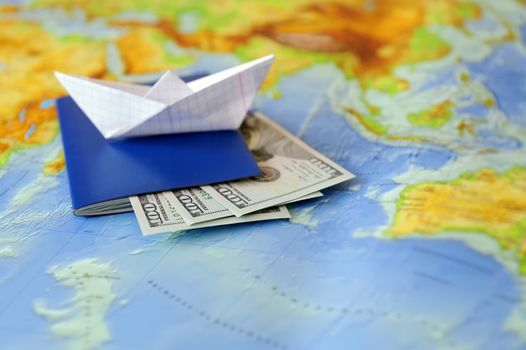 Paper boat, passport, money on a background map of the world. Traveling concept