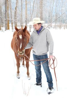 Young cowboy with his horse in a snow forest