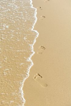 Foot steps and surf on tropical beach - abstract travel background