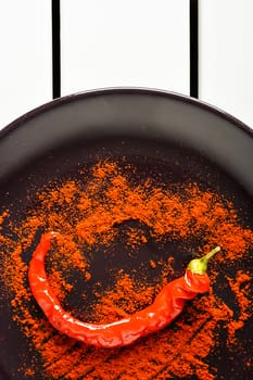 Red pepper with ground paprika on brown dish over white wood. Vertical image.