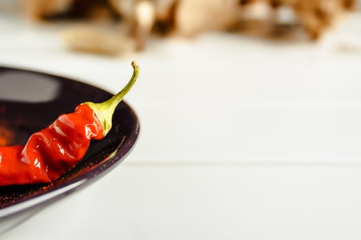 Closeup red pepper on brown dish over white wood. Horizontal image.