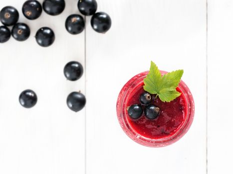 Delicious black currant smoothie in glass jar with fresh berries on white wood background. Top view or flat lay