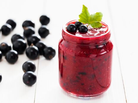 Delicious black currant smoothie or jam in glass jar with fresh berries on white wood background. Shallow DOF. Selective focus