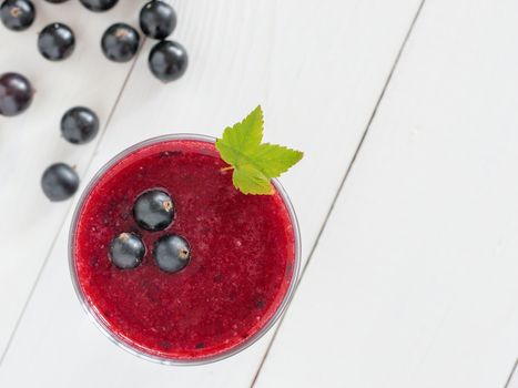 Delicious black currant smoothie with fresh berries on white wood background with copy space. Top view or flat lay