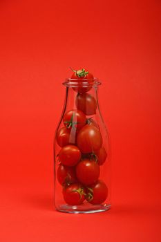 Big glass bottle full of cherry tomatoes over red background as symbol of fresh natural organic juice or ketchup