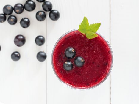 Delicious black currant smoothie with fresh berries on white wood background. Top view or flat lay