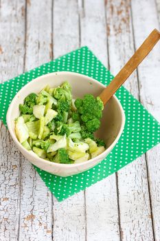 Salad in a deep bowl, broccoli, pepper and apple. On a wooden background