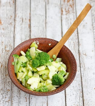 Salad in a deep bowl, broccoli, pepper and apple. On a wooden background
