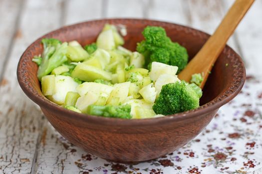 Salad in a deep bowl, broccoli, pepper and apple. On a wooden background