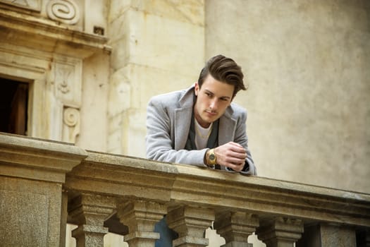 Elegant attractive young man outdoor wearing wool coat, in European city, looking away to a side