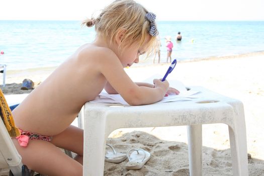 Cute baby girl drawing on the beach