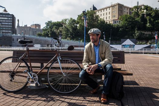 Middle-aged man with Irish beret sitting on a bench with his urban bike a sunny day