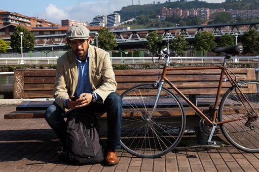 Middle-aged man with Irish beret sitting on a bench with his urban bike a sunny day