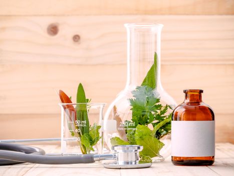 Alternative health care fresh herbal in laboratory glassware  with  stethoscope on wooden background.