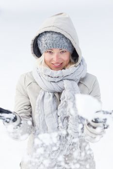 Cute casual young woman playing with snow in winter time.