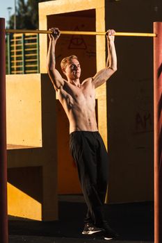 Young fit shirtless man exercising on outdoor sports ground. Concept: healthy lifestyle