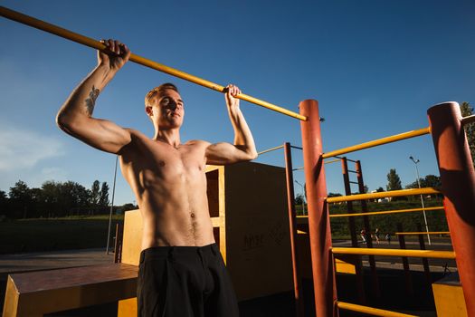 Young fit shirtless man exercising on outdoor sports ground. Concept: healthy lifestyle