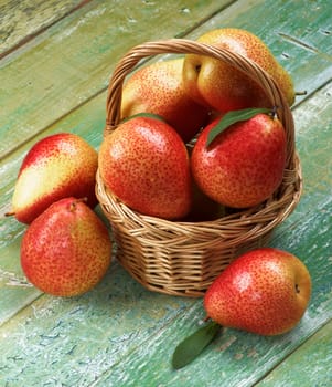 Arrangement of Ripe Yellow and Red Pears with Leafs in Wicker Basket closeup on Cracked Wooden background