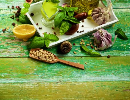 Freshly Made Creamy Pesto Sauce in Glass Gravy Boat with Ingredients, Spices and Olive Oil in White Wooden Tray as Frame on Cracked Wooden background