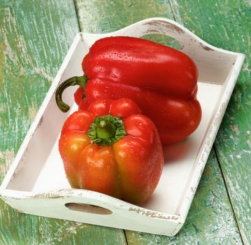 Fresh Ripe Red and Orange Bell Peppers in White Wooden Tray closeup on Green Wooden background