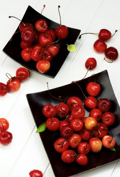 Arrangement of Fresh Ripe Sweet Maraschino Cherries in Black Wooden Plates closeup on Plank White background. Top View