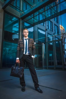 Young handsome successful stylish businessman standing near modern office building. Concept: victory.
