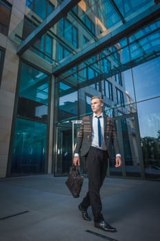 Young handsome successful stylish businessman walking near modern office building. Concept: victory.