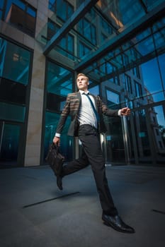 Young handsome successful stylish businessman running near modern office building. Concept: victory.