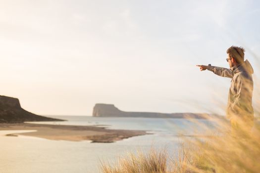Sporty active man pointing hand on island on horizon, enjoying beauty of nature, freedom and life at beautiful landscape. Active lifestyle outdoors.