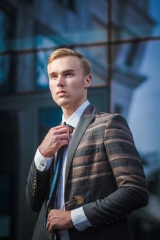 Young handsome successful stylish businessman standing near modern office building. Concept: victory.