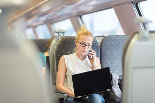 Businesswoman talking on cellphone and working on laptop while traveling by train. Business travel concept.