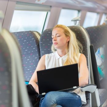 Businesswoman naping sitted while traveling by train and working on laptop. Tiresome business travel.