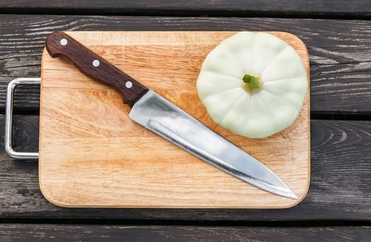 Squash on a cutting board on wooden background with a steel knife