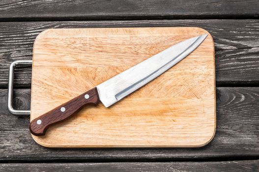 Steel knife on a cutting board on wooden background with