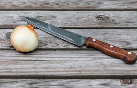 Knife,onion  on a table made of wooden planks