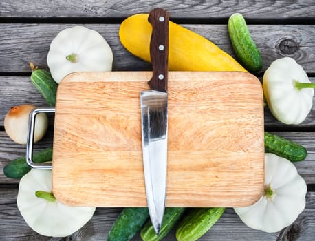 Cutting board, knife, fresh vegetables on wooden table.  Top view with copy space.