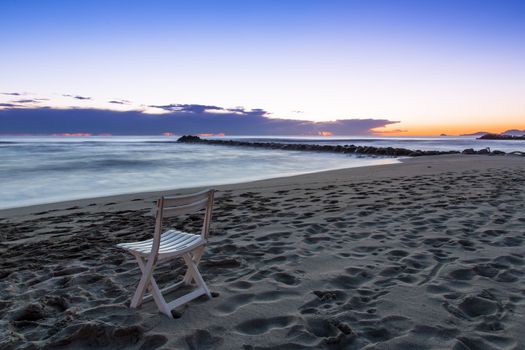 View of a chair on a beach of the Tuscan coast at sunset