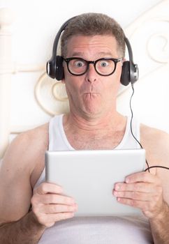 Funny man in bedroom with computer tablet and headphones