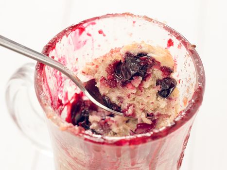 Mug Cake in glass mug with berries on white wooden background, close up