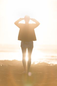 Silhouette of casualy dressed sporty woman watching sunset at the beach.