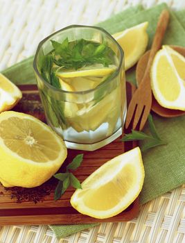 Delicious and Fresh Homemade Drink with Mint Leafs and Lemon Slices in Glass on Napkin closeup on Wicker background. Selective Focus
