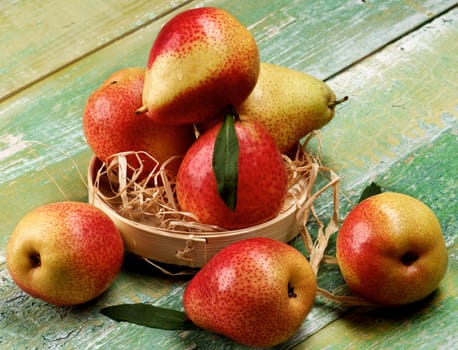 Arrangement of Ripe Yellow and Red Pears with Leafs in Wicker Bowl closeup on Cracked Wooden background