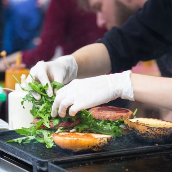 Chef making beef burgers outdoor on open kitchen international food festival event. Street food ready to serve on a food stall.